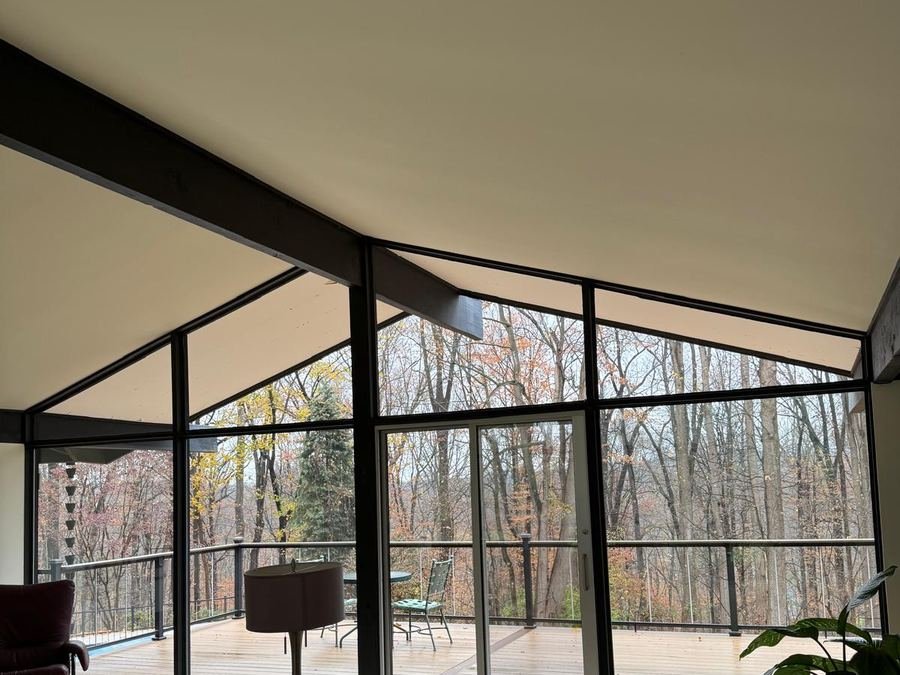A wall of floor-to-ceiling glass in a mid-century living room looking out onto woods