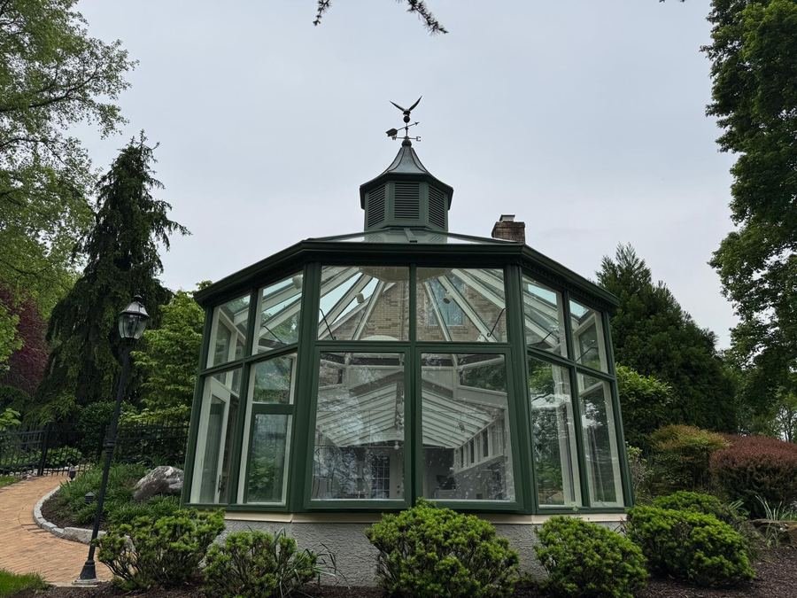 A green-framed garden conservatory with clear glass panels and a cupola