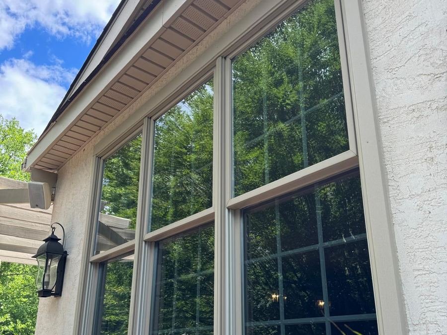 Tall casement windows on a stucco home reflecting trees and sky