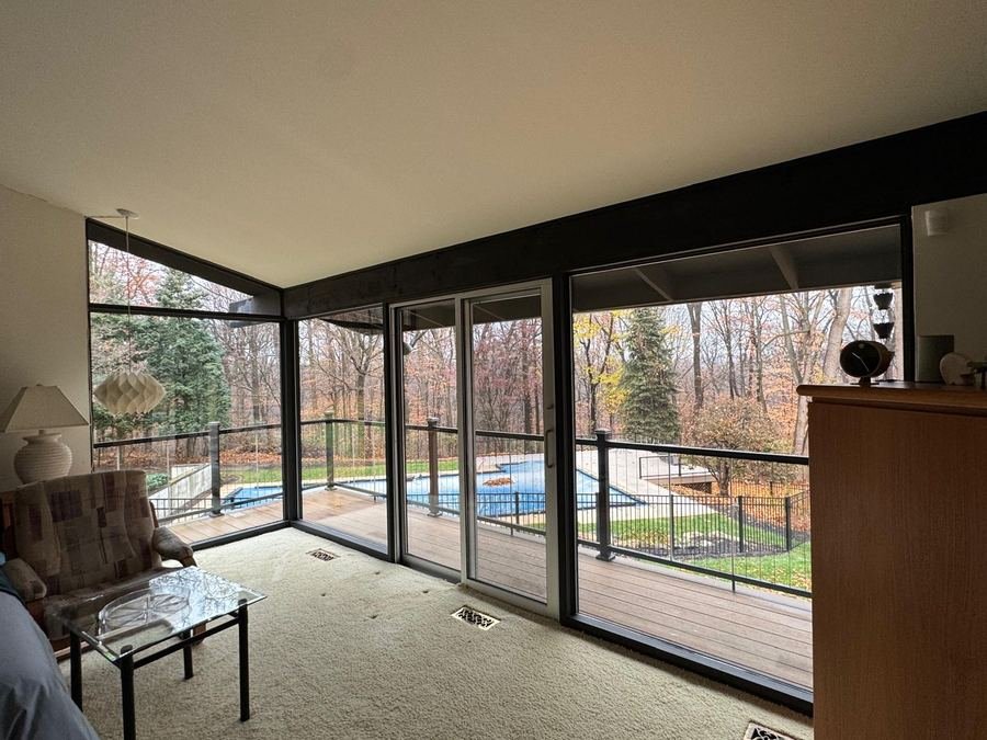 A sunroom with sliding glass doors looking out to a pool and deck